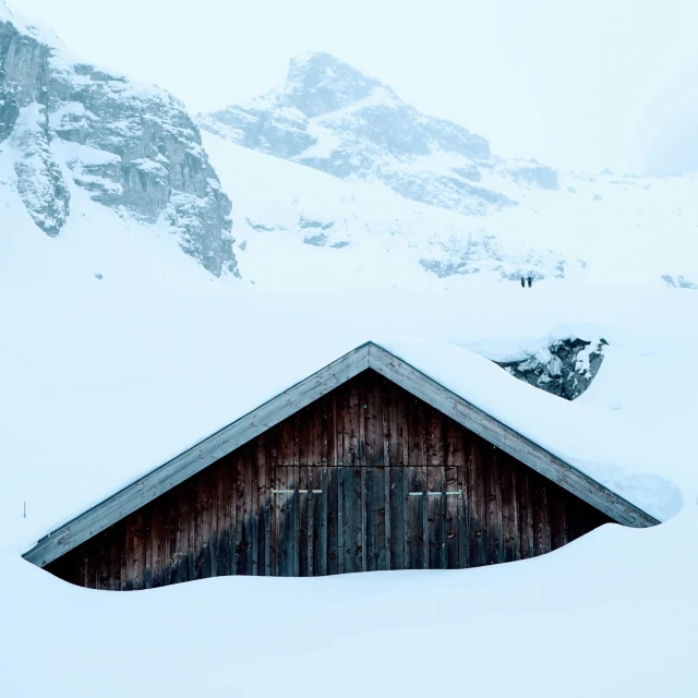 a snow covered hillside with a barn and mountains