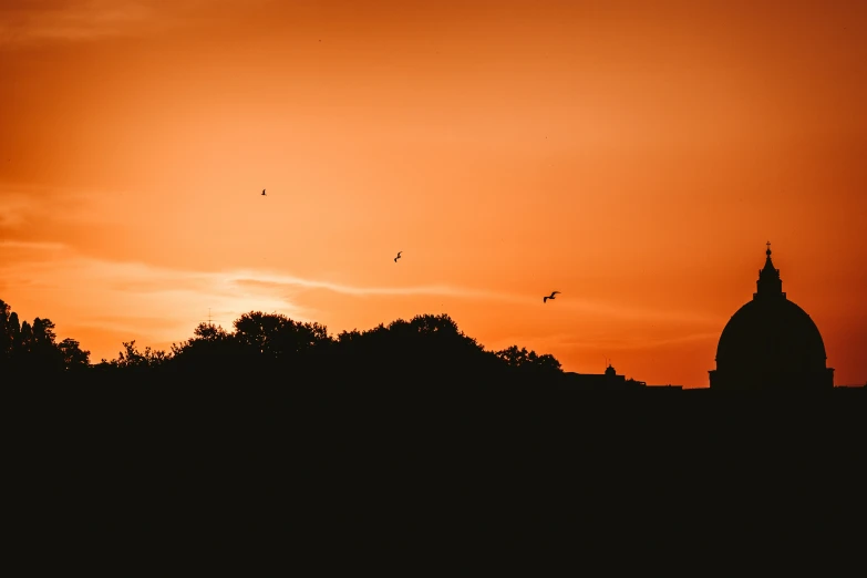 a sunset over some trees and a building