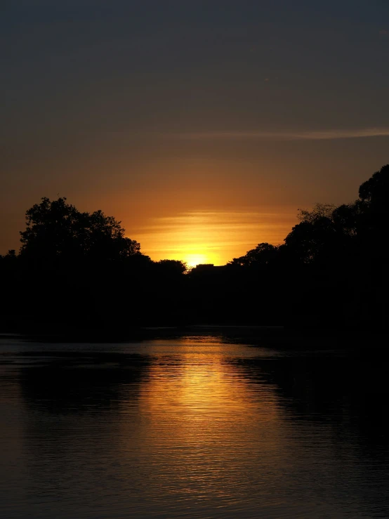 a sunset over the water with trees in the distance