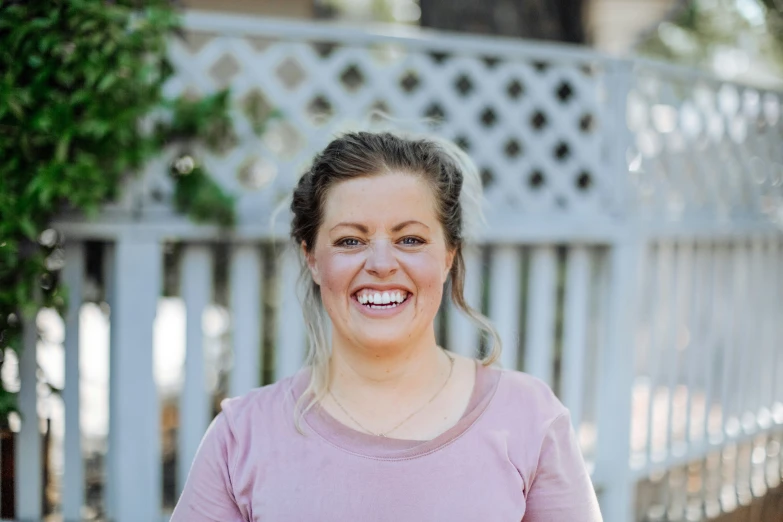 a smiling woman in a pink shirt is looking straight ahead