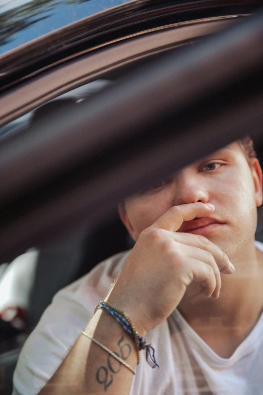 a man sitting in his car, holding his hand to his chin