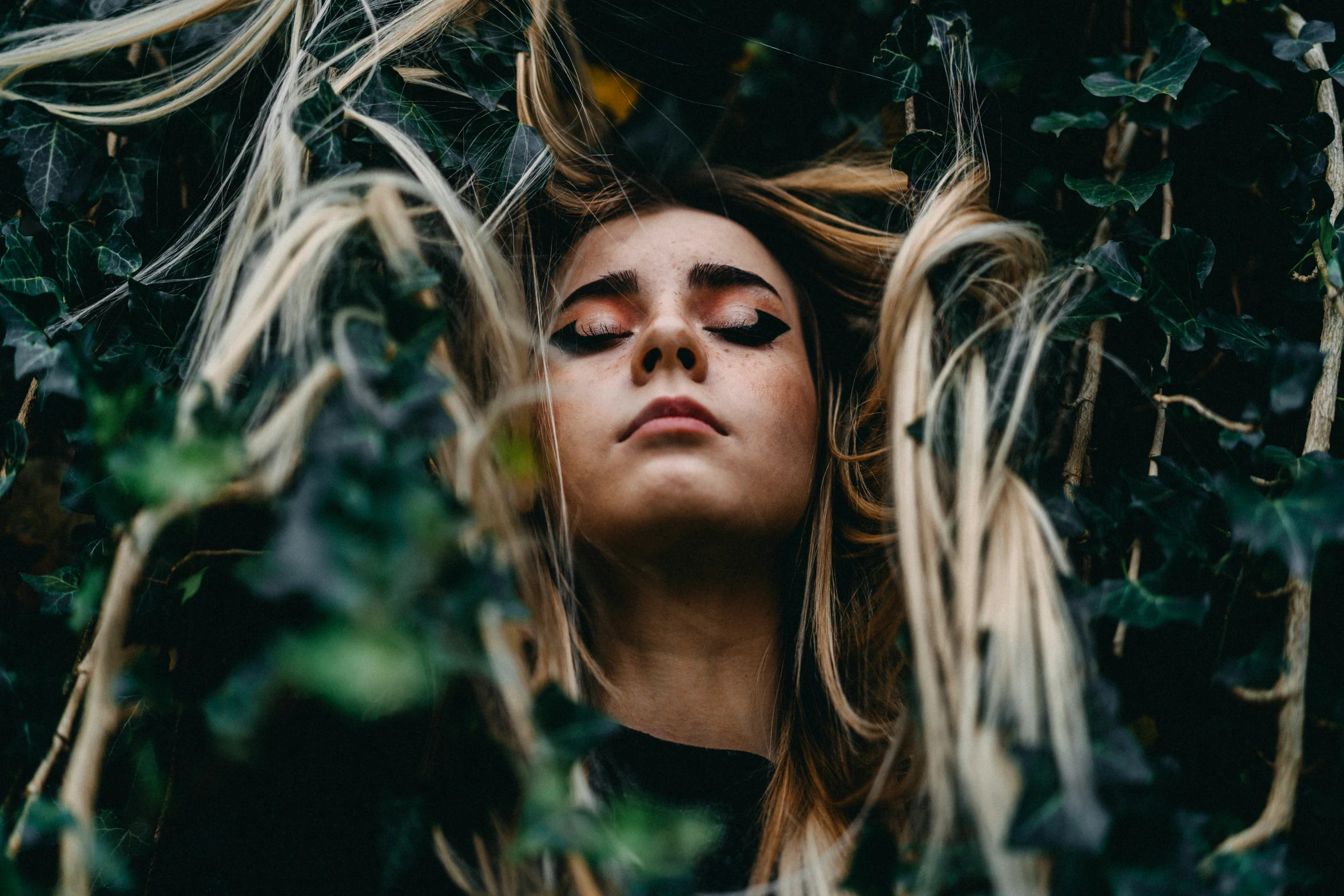 a woman is hiding in a bush with leaves on her head