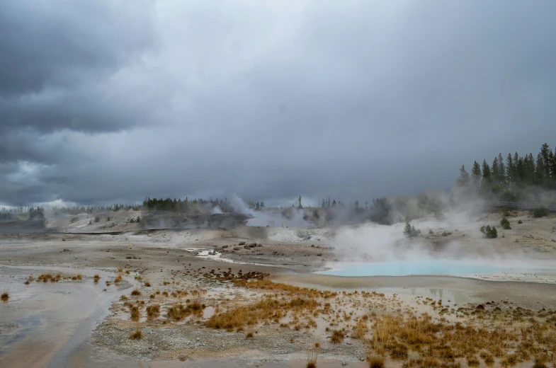 a geyser near a pool of water under a gray sky