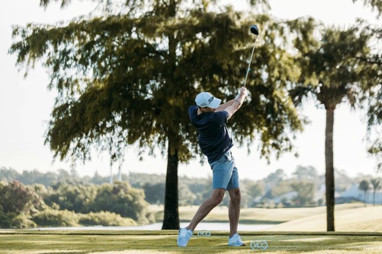 a man swinging a golf club in front of a tree