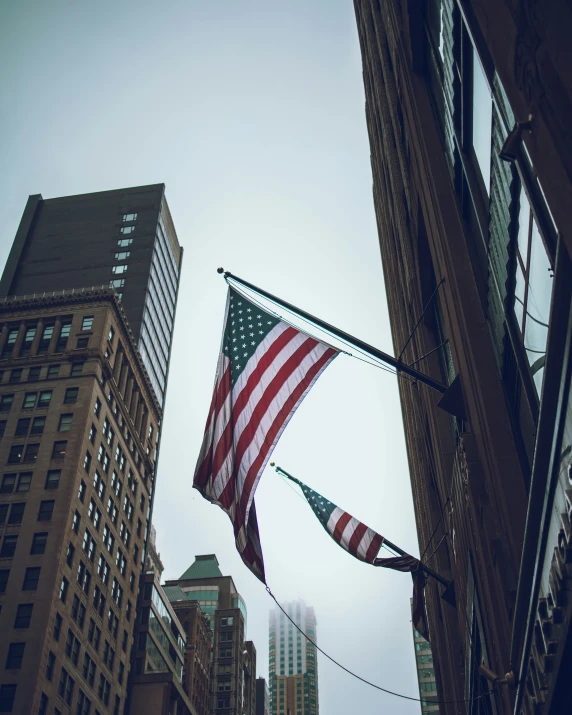 two american flags are flying in front of some tall buildings