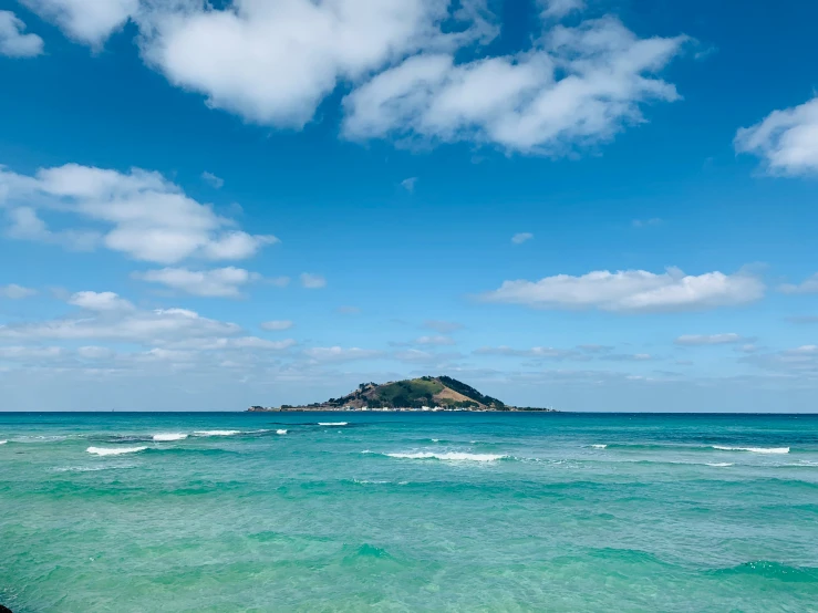 a view from the shore of the ocean, with a hill in the distance