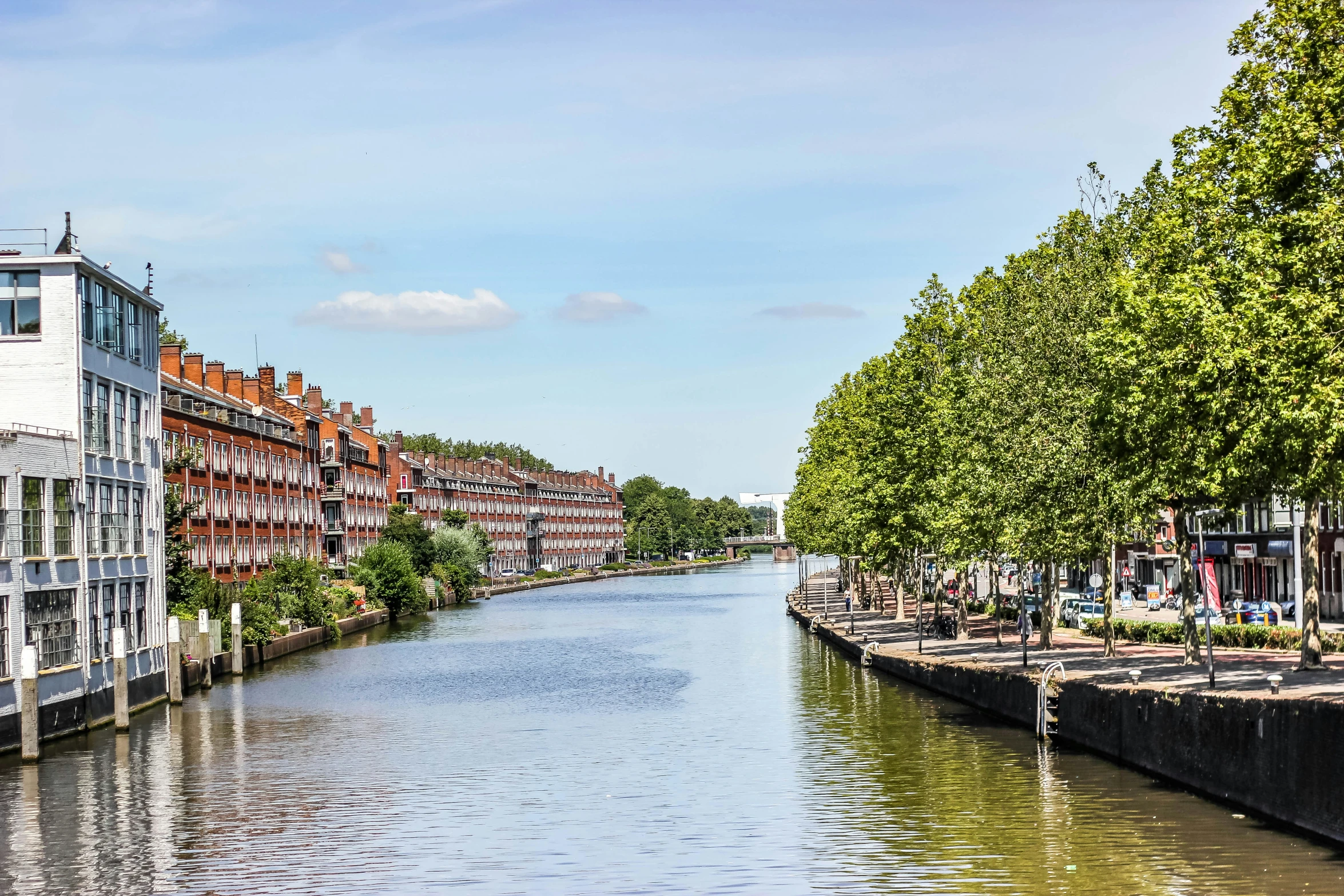 people walking down the side of a canal on an sunny day