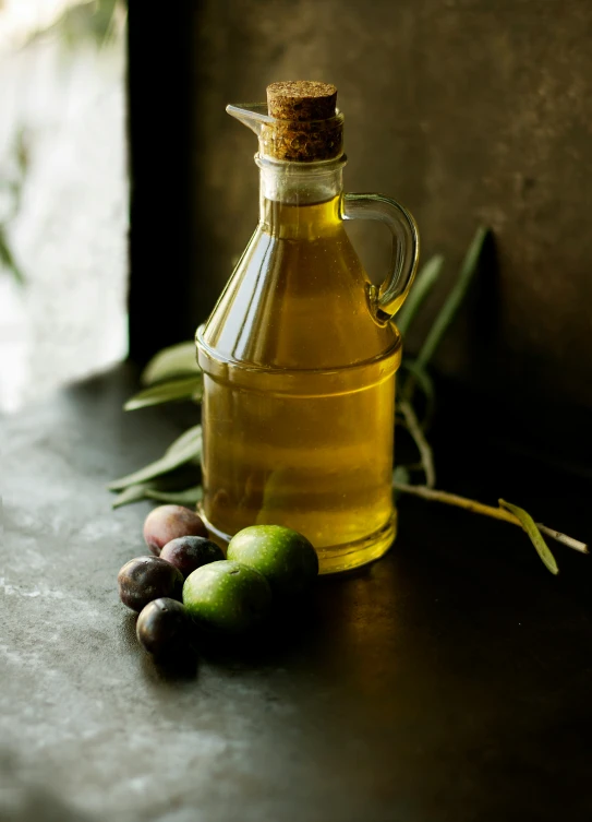 a bottle of olive oil sitting next to an olive nch and fruit