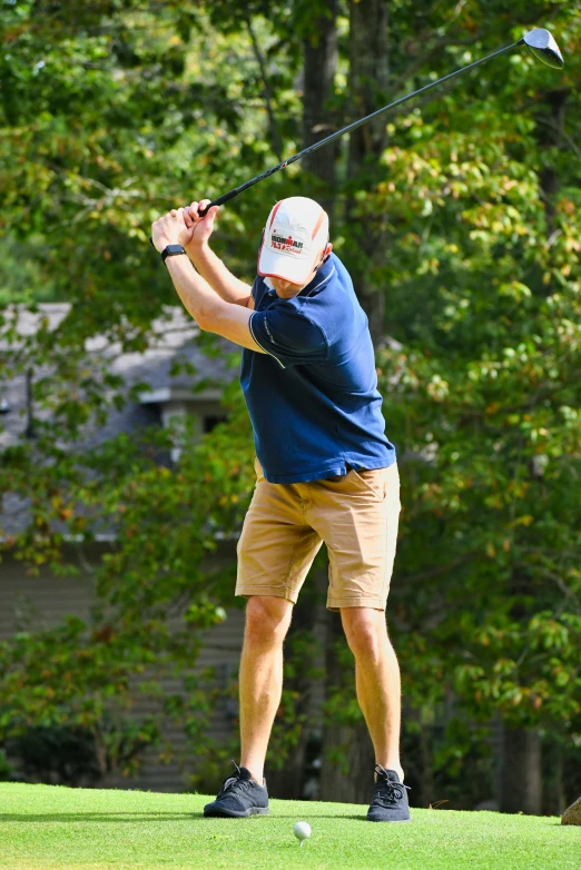 a man in shorts and a hat swings a golf club