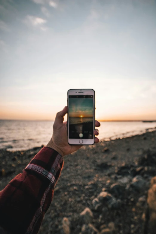 a man holding his phone up for a po with the sea in the background