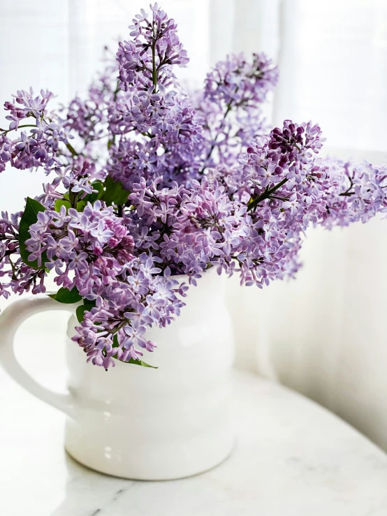 a white vase filled with purple flowers on a table