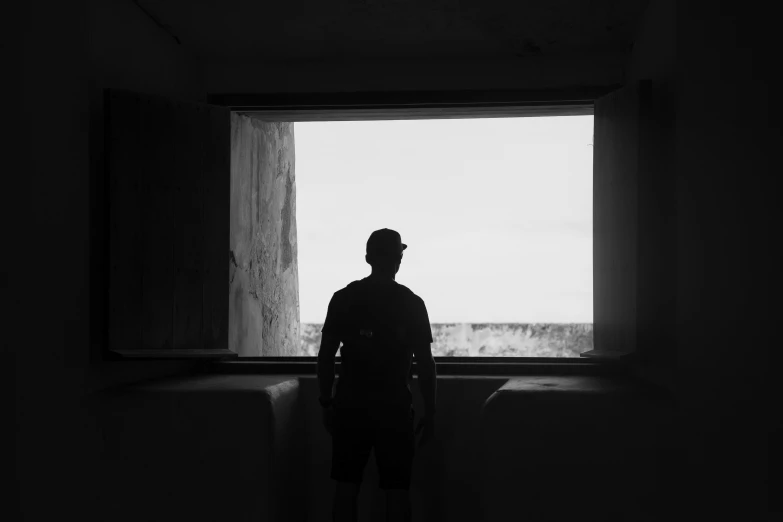 a man stands inside an unfinished room looking out the window