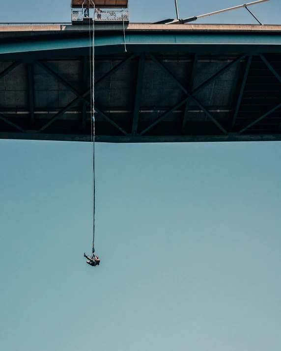 man hanging onto an electrical cable while being suspended on top of an overhead structure
