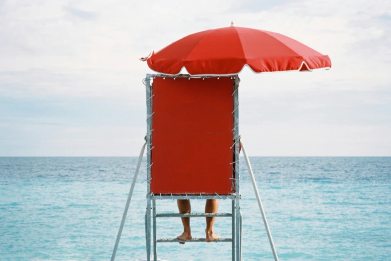 the person is sitting on a red towel under the red umbrella