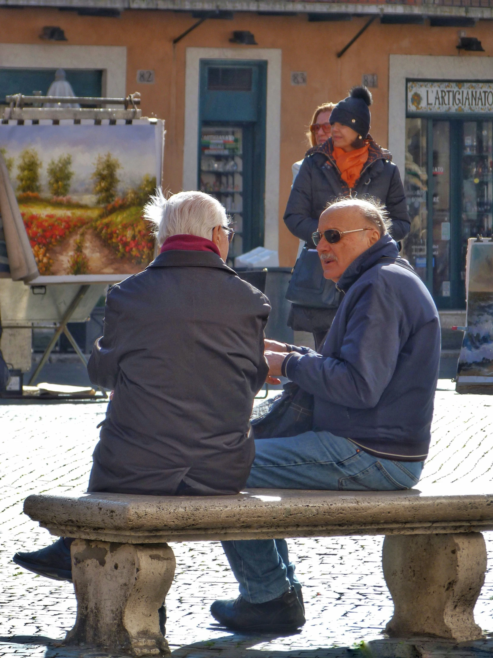 two men sitting on a bench outside and an older man talking to them