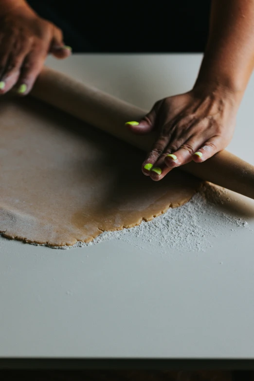 two hands rolling dough on top of an unfinished surface