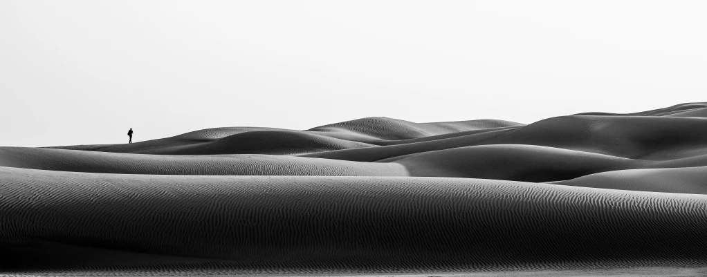 a lone figure is seen in the distance amongst many large dunes