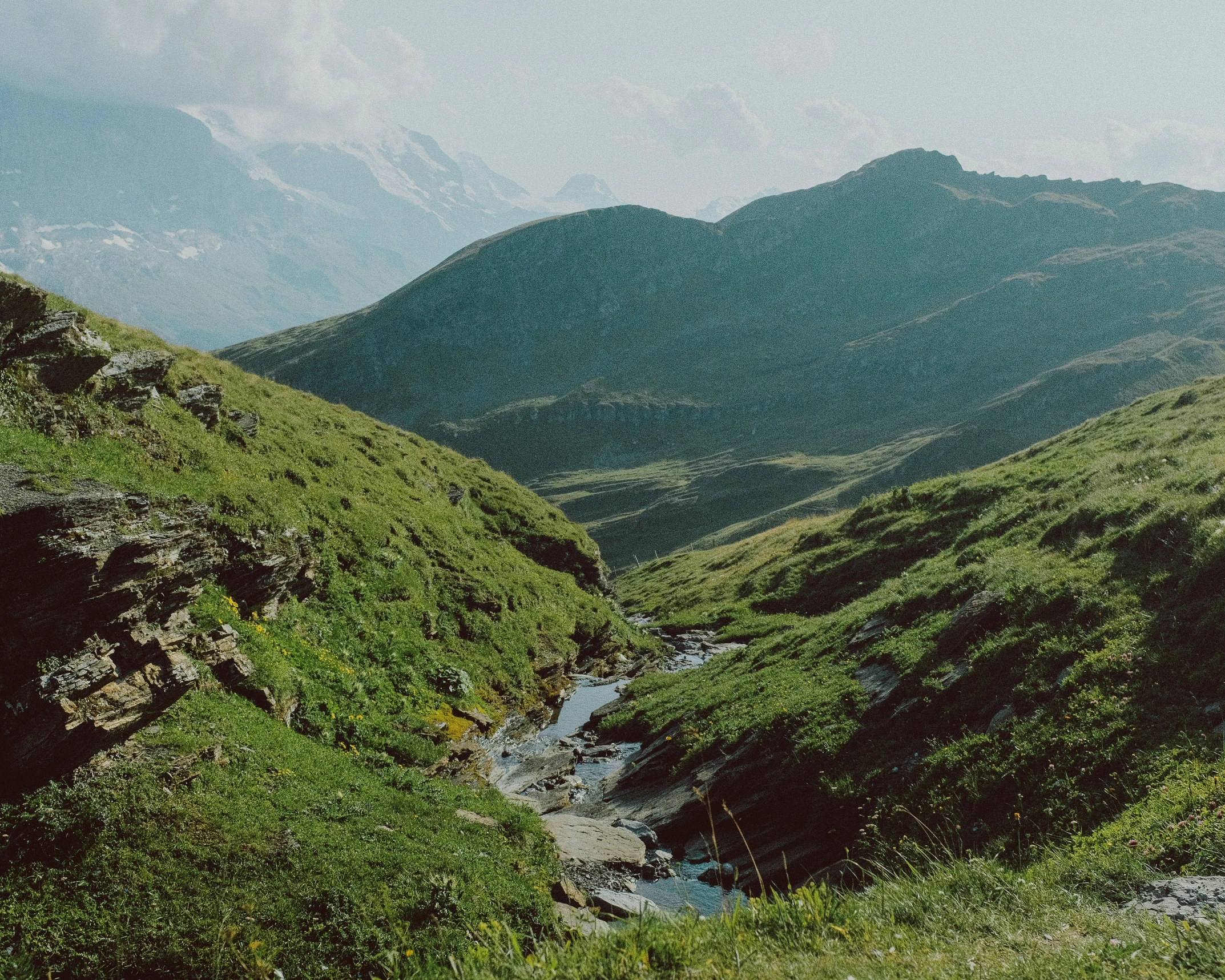 the valley in the middle of the mountains is covered with green grass