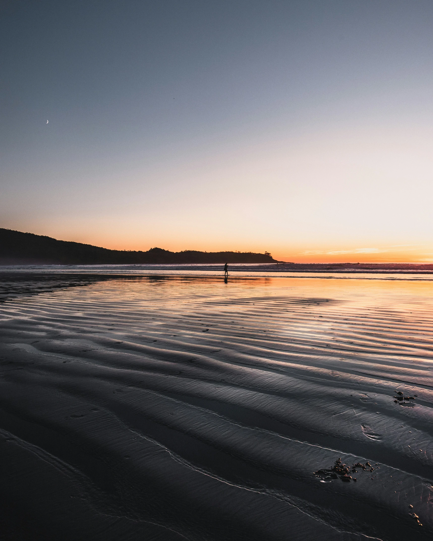 a beach at sunset with the sun rising behind a hill