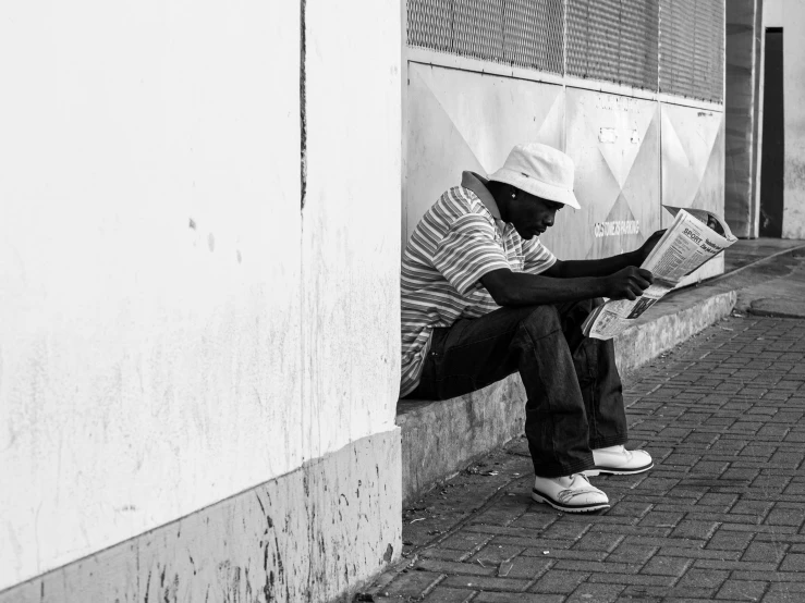 the man is reading a newspaper while sitting in front of the wall