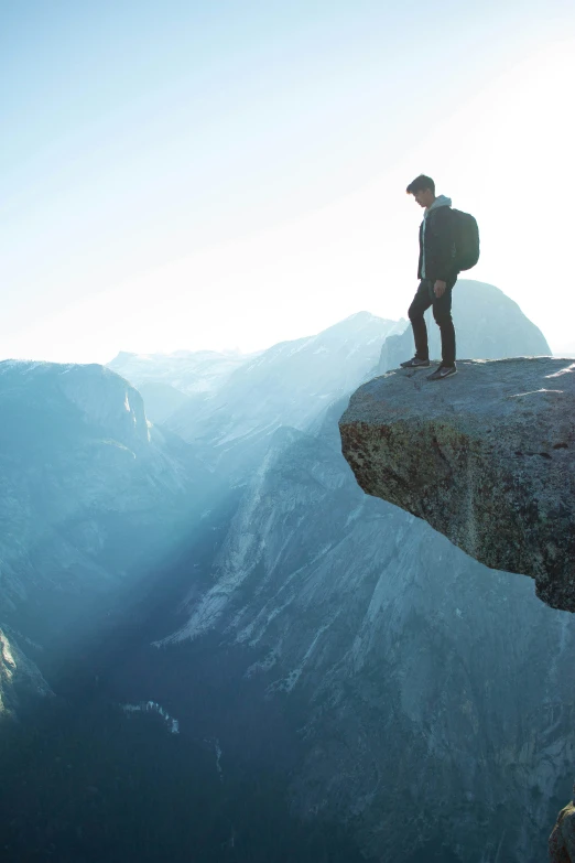 a man in black hat on cliff overlooking mountains