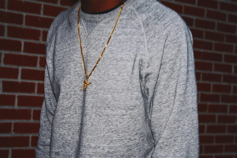 a man with necklace standing in front of a brick wall