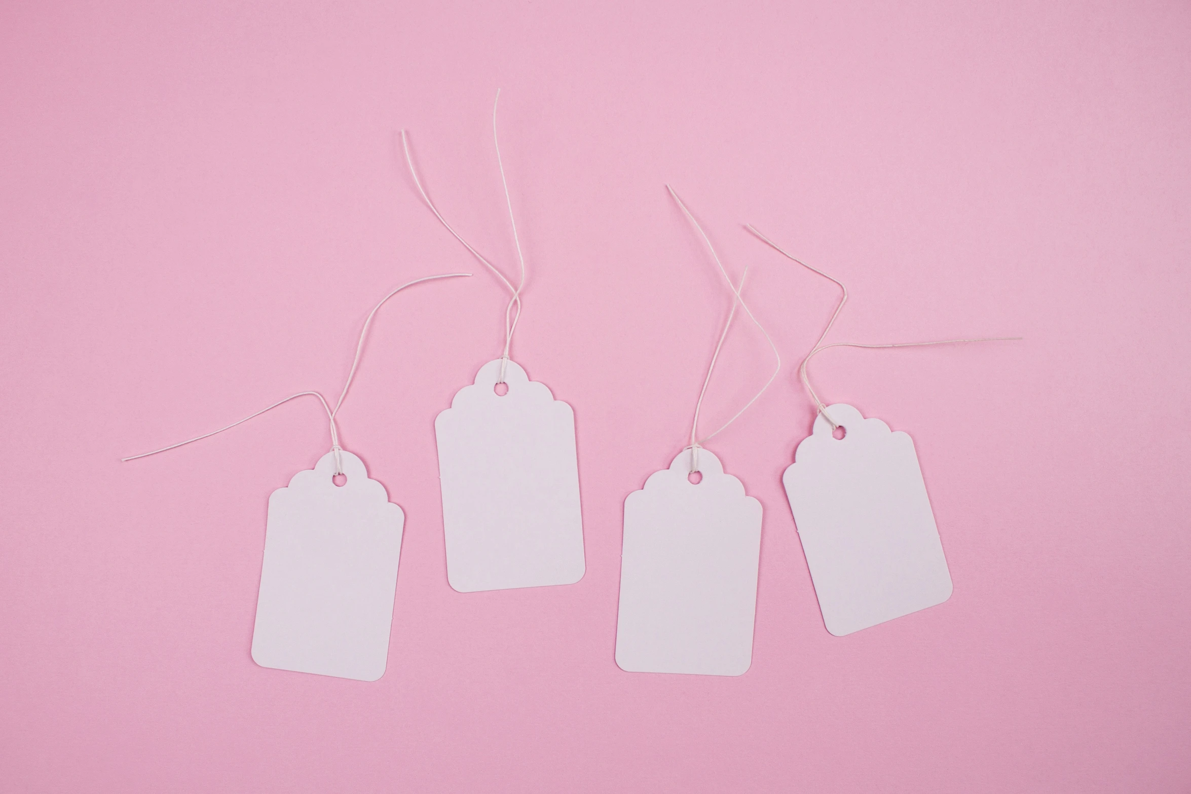 four tags attached to white string against a pink backdrop