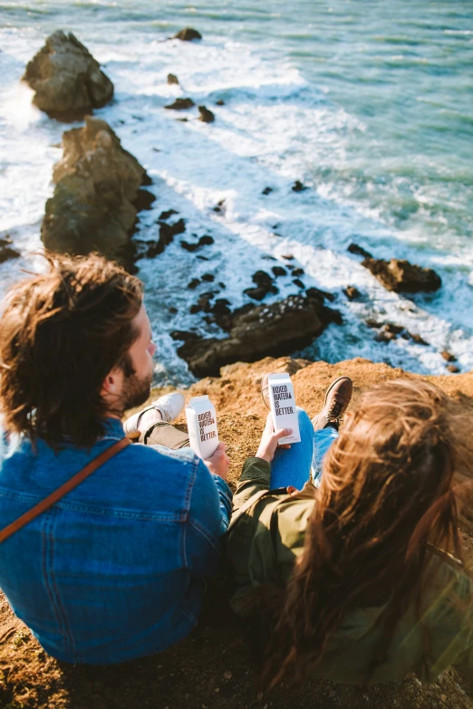 a couple sit on the edge of a cliff near the ocean