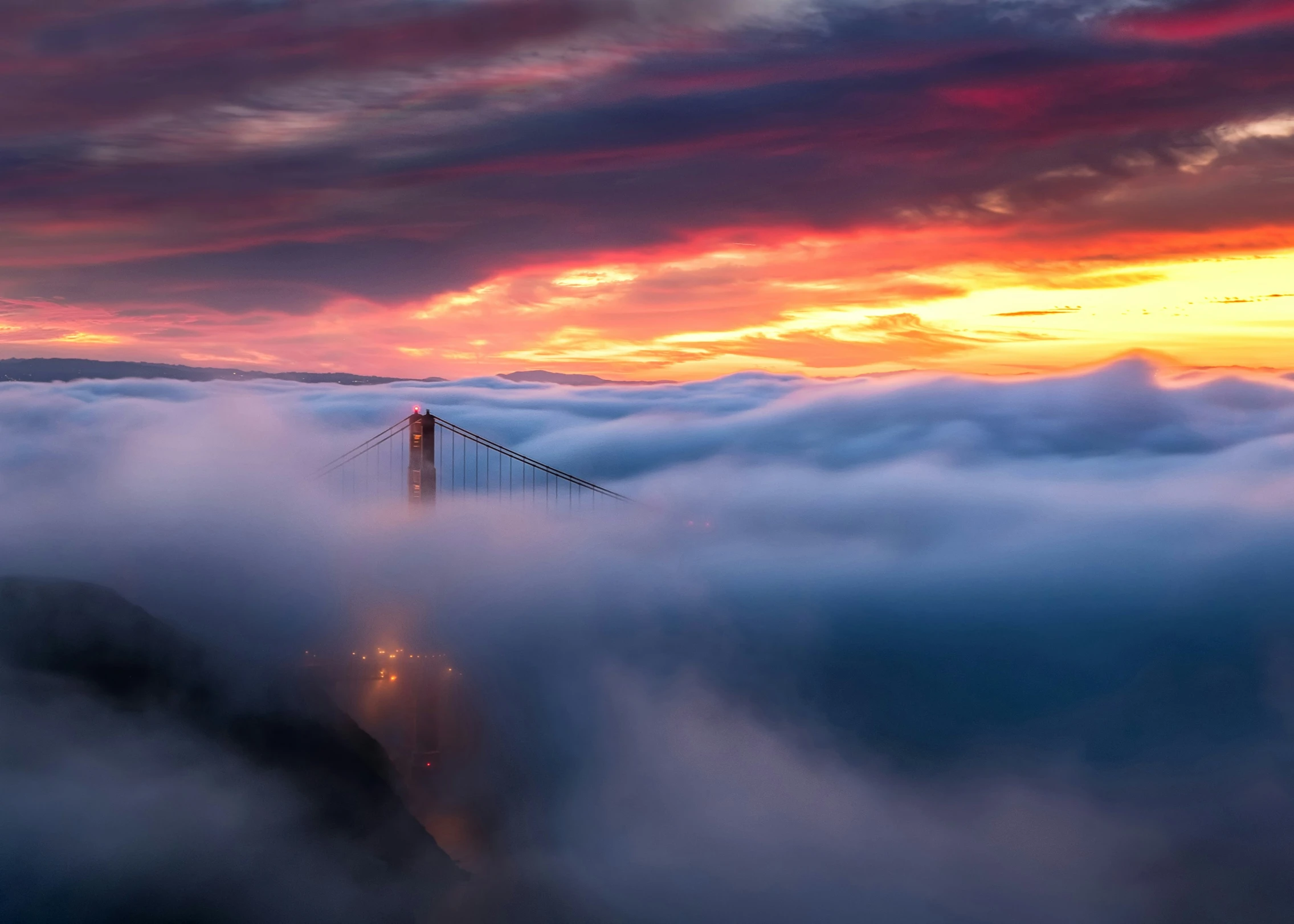 a large fog bank at sunset with a bridge on top