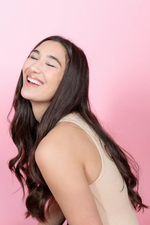 a woman with long hair and smiling wearing a tan tank top