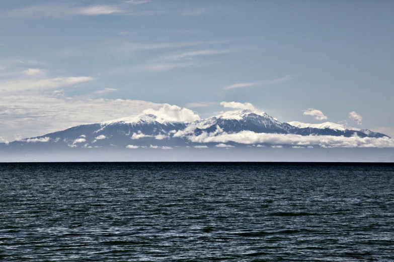 the large mountains are covered with clouds next to the water