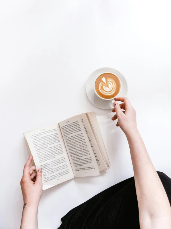 hands that are holding a book and reading a cup of coffee