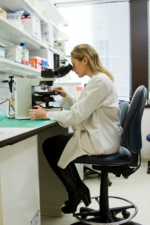 a woman wearing a white coat and knee high boots is examining an item