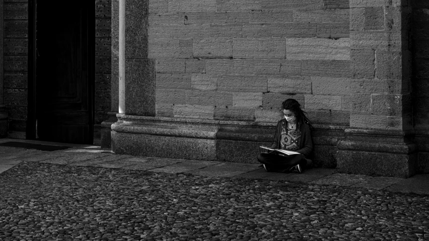 a woman sitting against a wall near an entrance