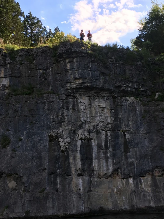two people are standing on the ledge of a large rock face