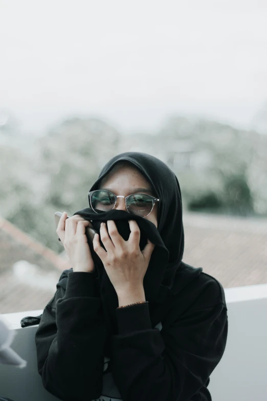 a hooded woman wearing sunglasses holding up soing