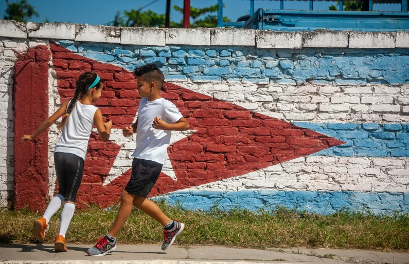 a boy and a girl run near a colorful painted brick wall