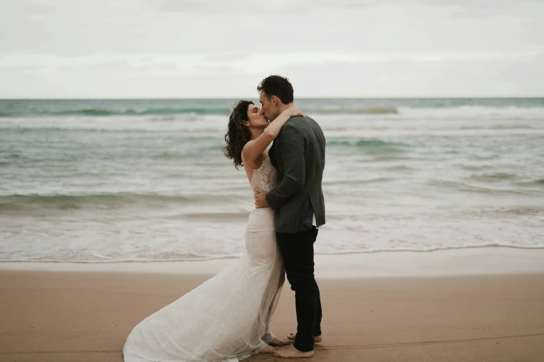 two people that are kissing and standing in the sand