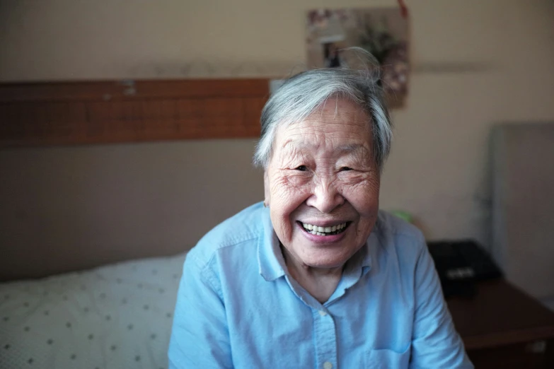 an elderly person smiles while sitting on a bed