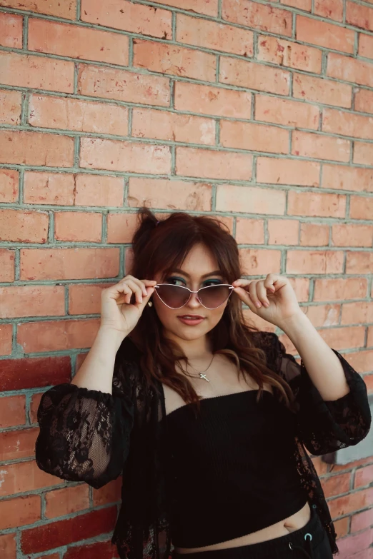 a woman is posing by the wall wearing shades