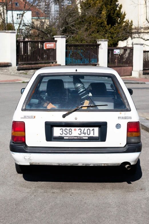 a white small car in parking lot with a brown dog sitting inside the rear window