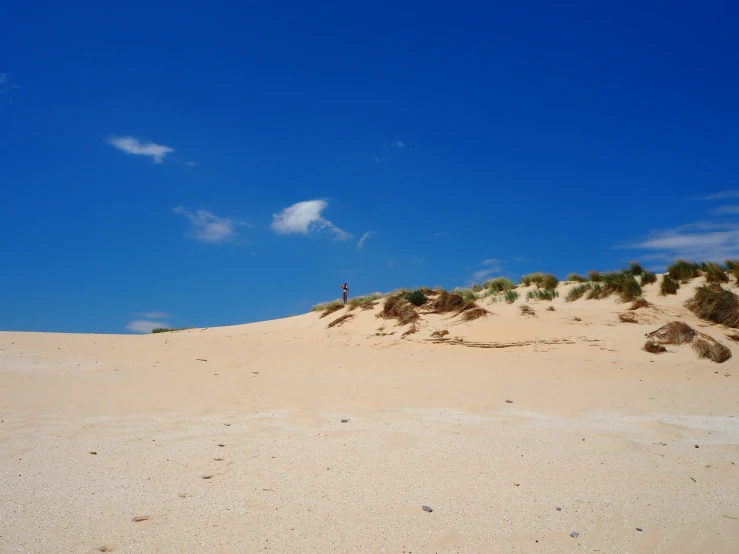 a single surfer is in the distance as he walks up a dune
