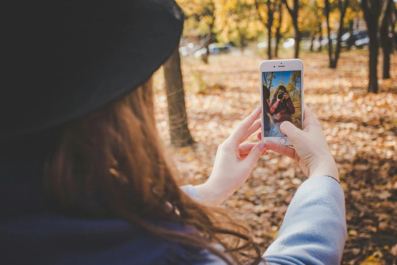 a woman taking a po of leaves on the ground with her phone