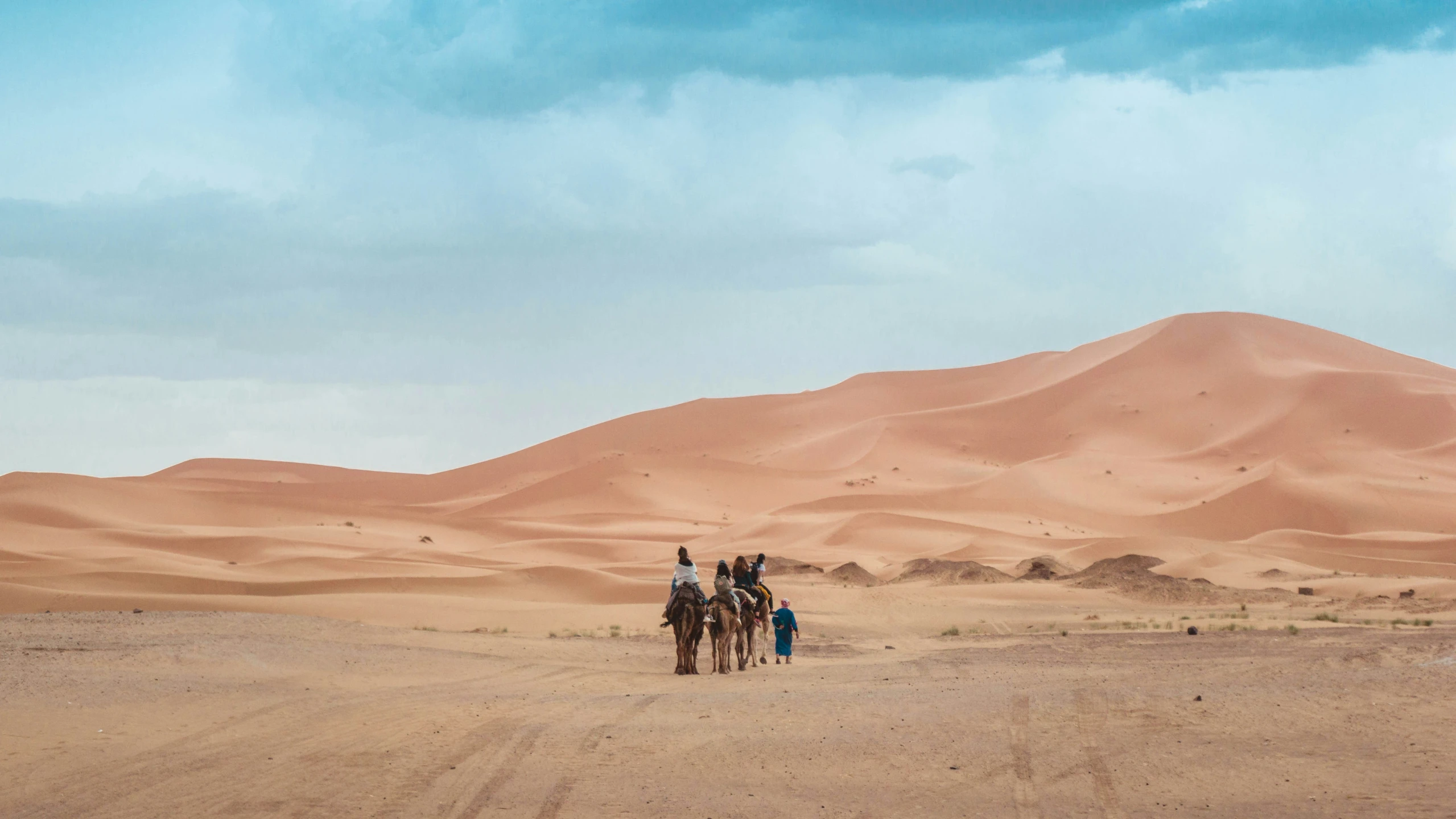 three people ride on horses in the desert