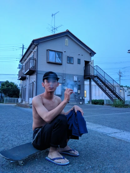 a man in sandals sits with his shirt off and a skateboard