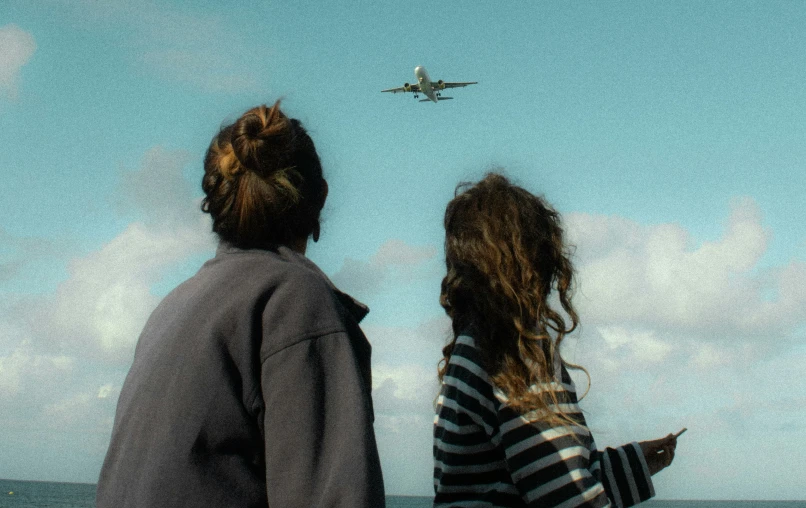two people in front of an airplane flying low in the sky