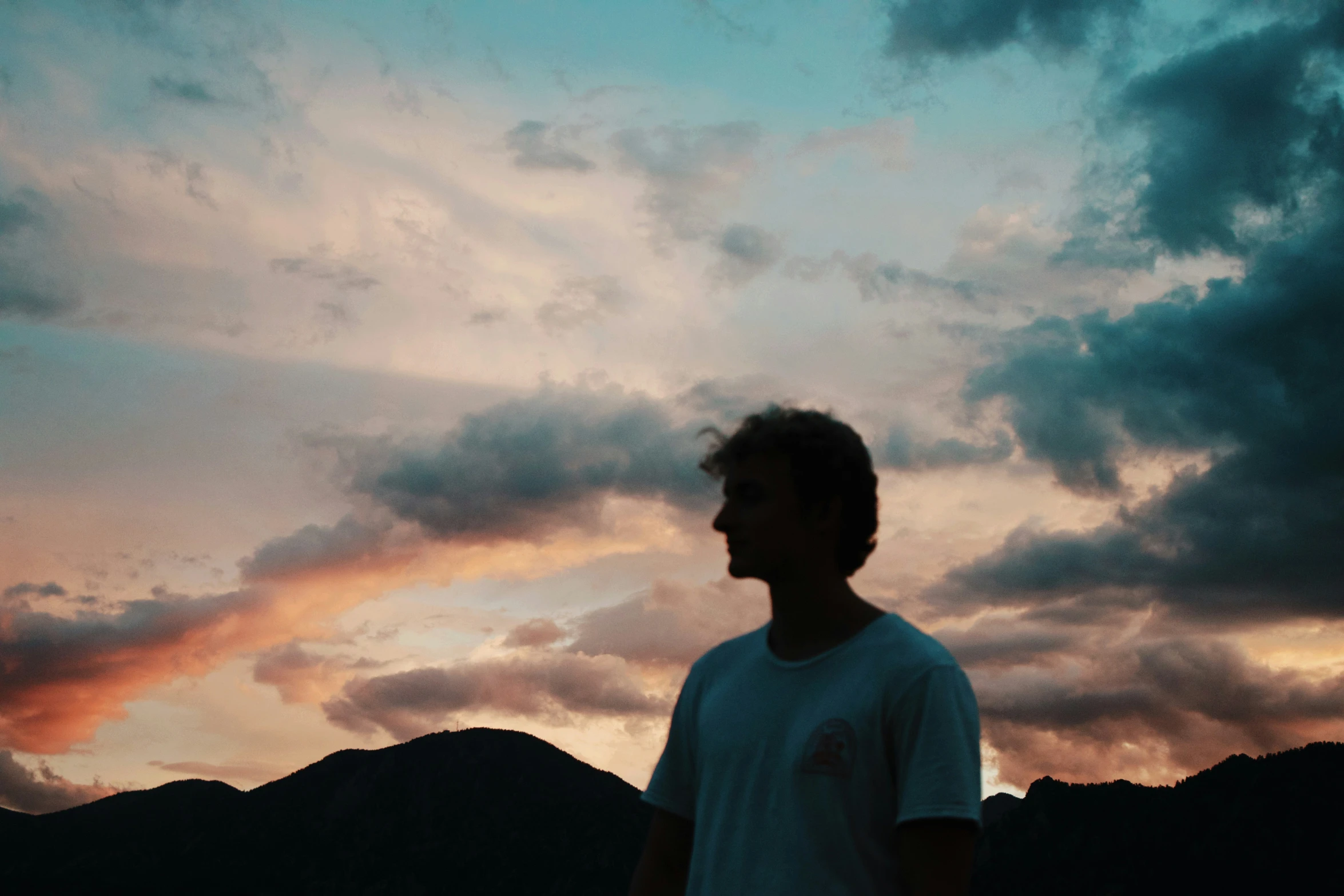 a man is looking down at the ground as clouds cover mountains in the background