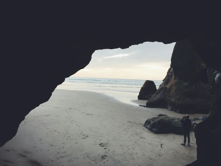 man standing in a cave near the beach on an overcast day