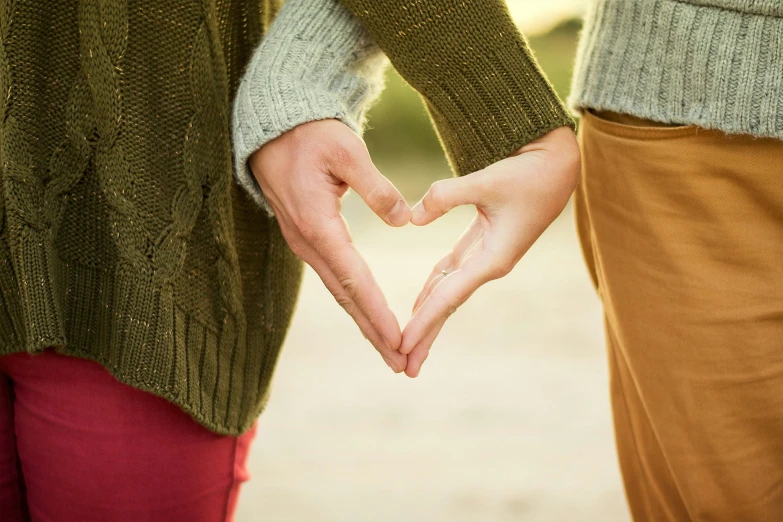 two people in green sweaters and red pants hold hands making a heart