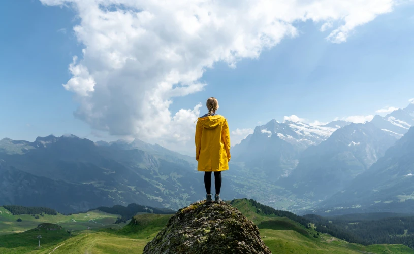 a woman in a yellow rain coat standing on top of a mountain